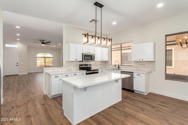 kitchen featuring stainless steel appliances, kitchen peninsula, pendant lighting, white cabinets, and ceiling fan with notable chandelier