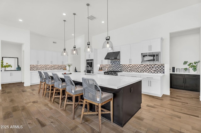 20716 E Pummelos Rd, Queen Creek, AZ 85142 - kitchen featuring appliances with stainless steel finishes, under cabinet range hood, tasteful backsplash, light wood-style flooring, and light countertops