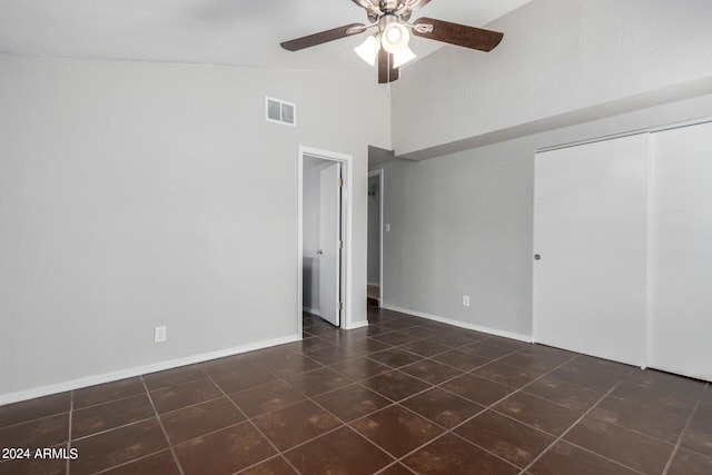 unfurnished bedroom with high vaulted ceiling, a closet, ceiling fan, and dark tile patterned flooring