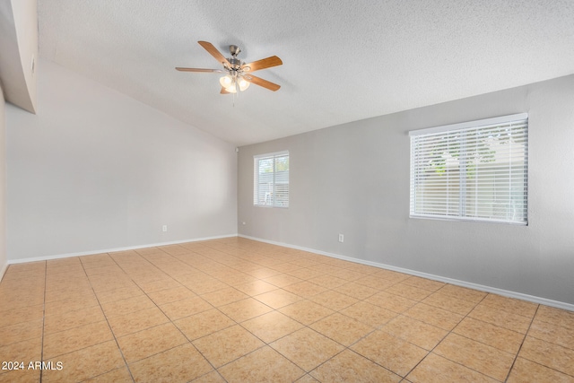 spare room with a textured ceiling, light tile patterned flooring, vaulted ceiling, and ceiling fan