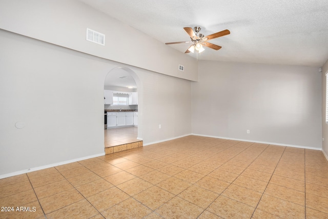 empty room featuring ceiling fan, light tile patterned floors, a textured ceiling, and vaulted ceiling