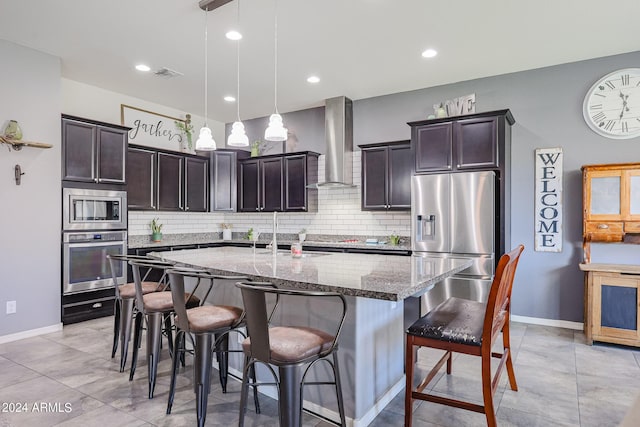 kitchen with light stone countertops, hanging light fixtures, sink, stainless steel appliances, and wall chimney exhaust hood