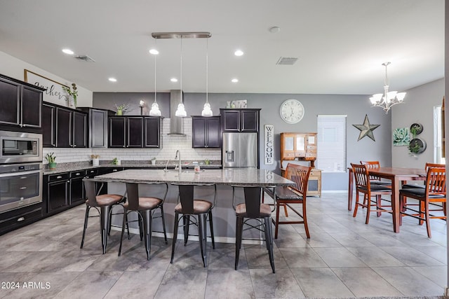 kitchen with decorative light fixtures, sink, a kitchen island with sink, wall chimney range hood, and stainless steel appliances