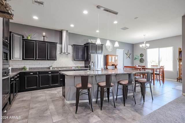 kitchen featuring pendant lighting, a breakfast bar, stainless steel appliances, a center island with sink, and wall chimney exhaust hood