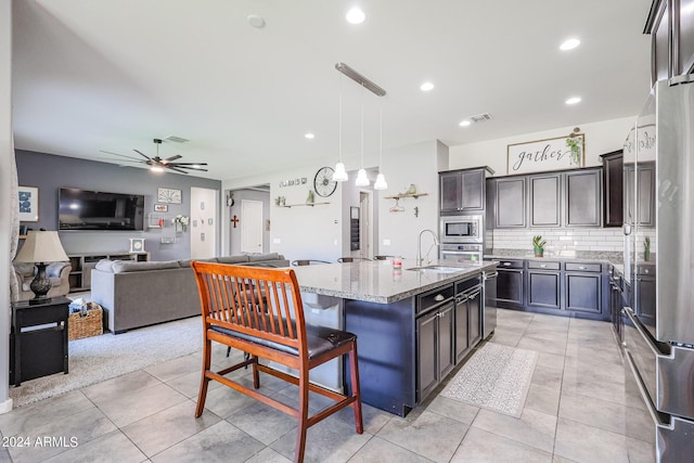 kitchen with a kitchen bar, appliances with stainless steel finishes, hanging light fixtures, a kitchen island with sink, and sink