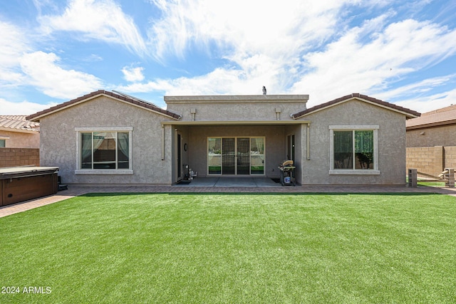 rear view of property with a lawn, a hot tub, and a patio