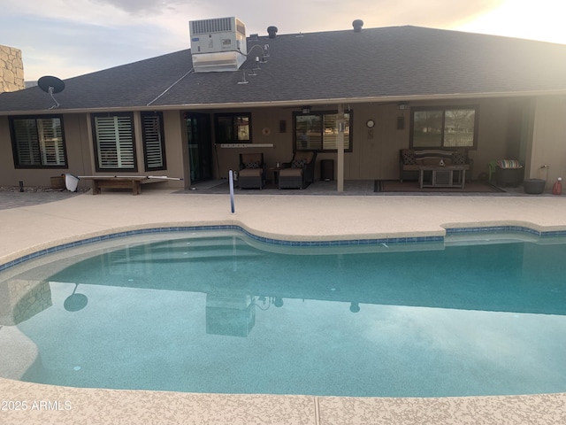 pool at dusk featuring an outdoor pool, a patio, and central AC unit