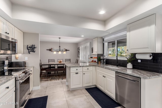 kitchen with light stone counters, stainless steel appliances, hanging light fixtures, white cabinetry, and a peninsula