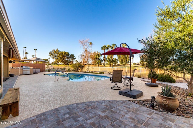 view of swimming pool featuring a patio area, a fenced backyard, and an outdoor kitchen