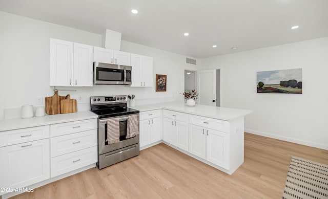 kitchen with appliances with stainless steel finishes, kitchen peninsula, light hardwood / wood-style flooring, and white cabinets