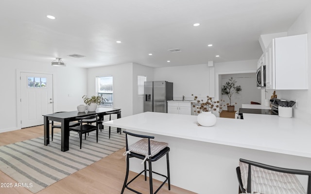 kitchen featuring light hardwood / wood-style flooring, a kitchen breakfast bar, stainless steel appliances, white cabinets, and kitchen peninsula