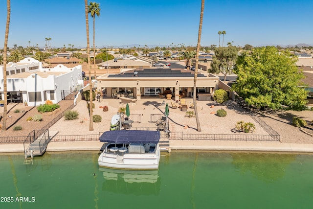 rear view of property with roof mounted solar panels, a fenced backyard, a patio, and a water view