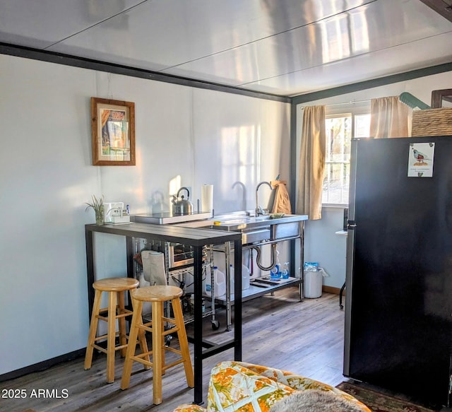 kitchen featuring a sink, wood finished floors, freestanding refrigerator, and baseboards