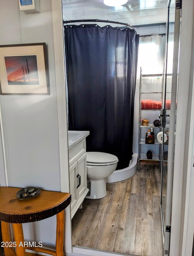 full bathroom featuring toilet, a shower with shower curtain, wood finished floors, and vanity