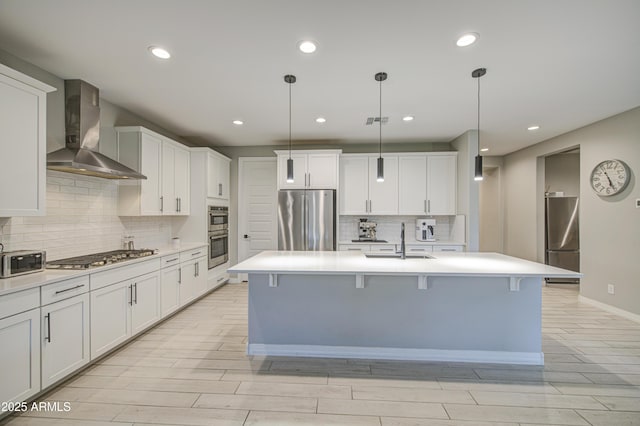 12806 W Mclellan Rd, Glendale, AZ 85307 - kitchen with stainless steel appliances, wall chimney exhaust hood, wood finish floors, light countertops, and a kitchen island with sink