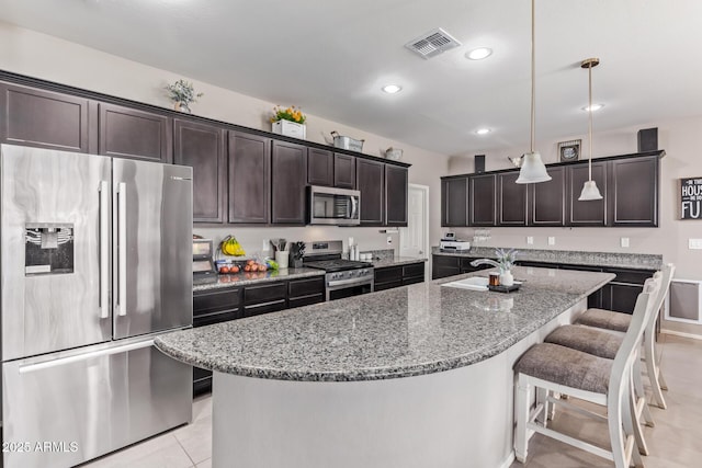 kitchen with appliances with stainless steel finishes, a kitchen island with sink, dark brown cabinetry, and decorative light fixtures