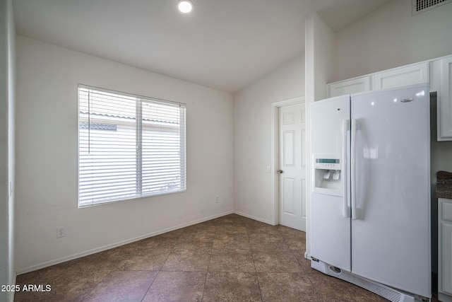 kitchen with visible vents, dark countertops, white cabinets, vaulted ceiling, and white fridge with ice dispenser