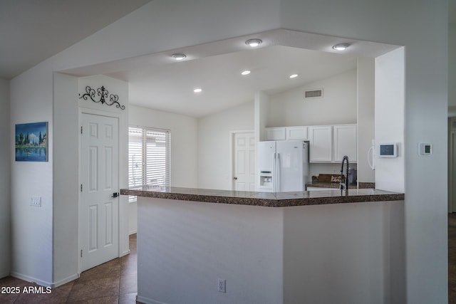kitchen featuring visible vents, a peninsula, lofted ceiling, white fridge with ice dispenser, and white cabinetry