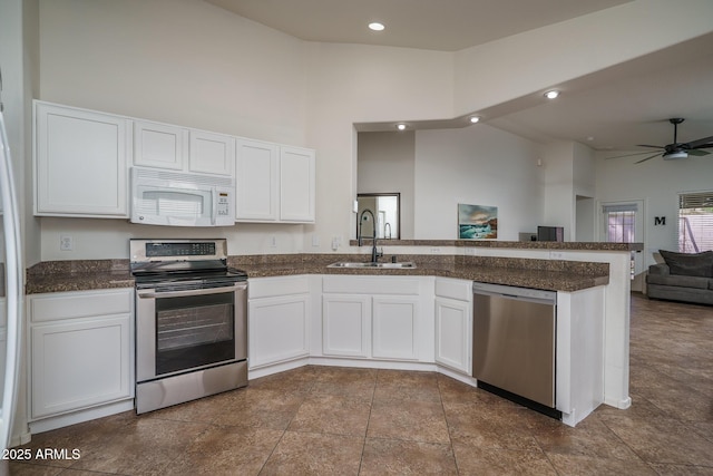 kitchen featuring a peninsula, dark countertops, white cabinets, a sink, and stainless steel appliances