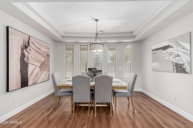 dining area featuring a raised ceiling, visible vents, baseboards, and wood finished floors