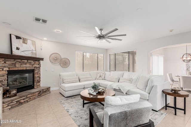 living area featuring visible vents, arched walkways, light tile patterned flooring, a stone fireplace, and recessed lighting