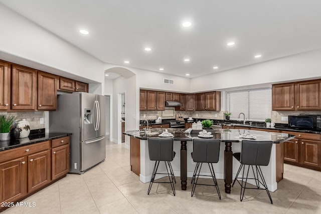 kitchen with arched walkways, appliances with stainless steel finishes, a breakfast bar area, a kitchen island with sink, and under cabinet range hood