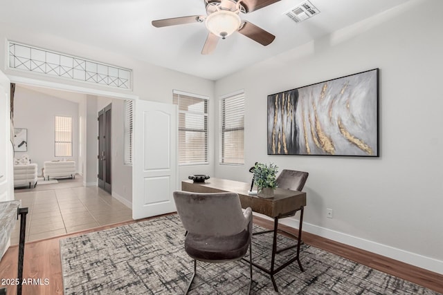 home office with a ceiling fan, wood finished floors, visible vents, and baseboards