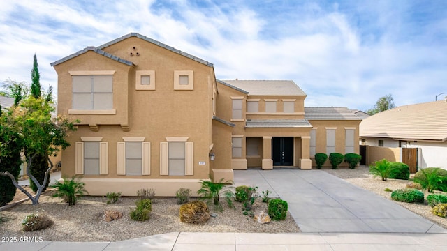 view of front of house featuring driveway, fence, a tiled roof, and stucco siding