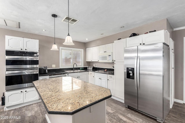 kitchen with white cabinets, a sink, stainless steel appliances, wood finished floors, and visible vents