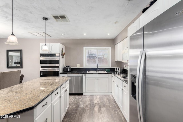 kitchen featuring white cabinets, a sink, stainless steel appliances, wood finished floors, and visible vents