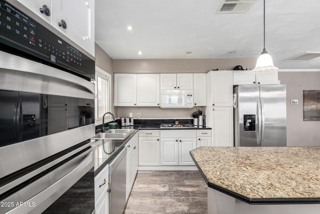 kitchen featuring visible vents, appliances with stainless steel finishes, wood finished floors, a sink, and white cabinetry