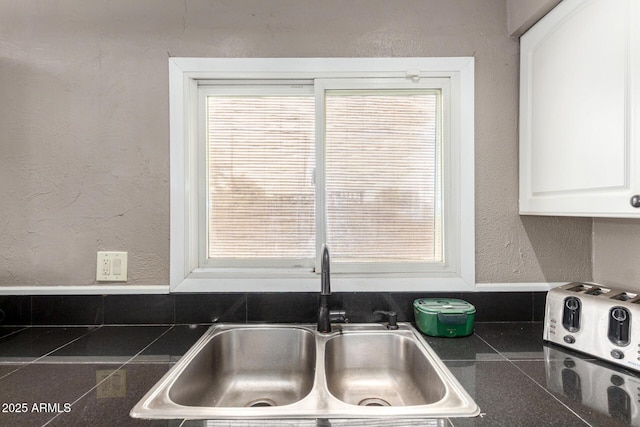 room details featuring a sink, tile counters, a textured wall, and white cabinetry