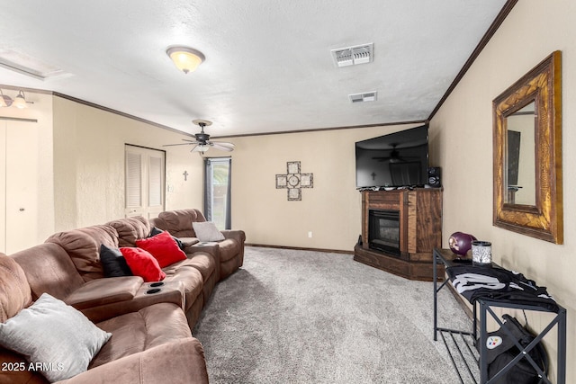 living area with visible vents, crown molding, carpet floors, a glass covered fireplace, and a ceiling fan