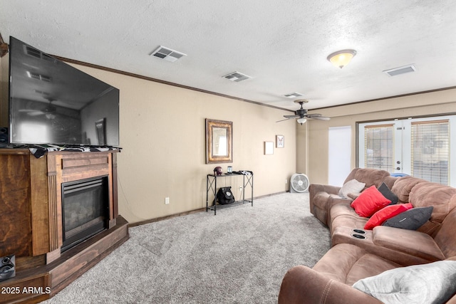 carpeted living room with visible vents, a textured ceiling, a glass covered fireplace, and ceiling fan