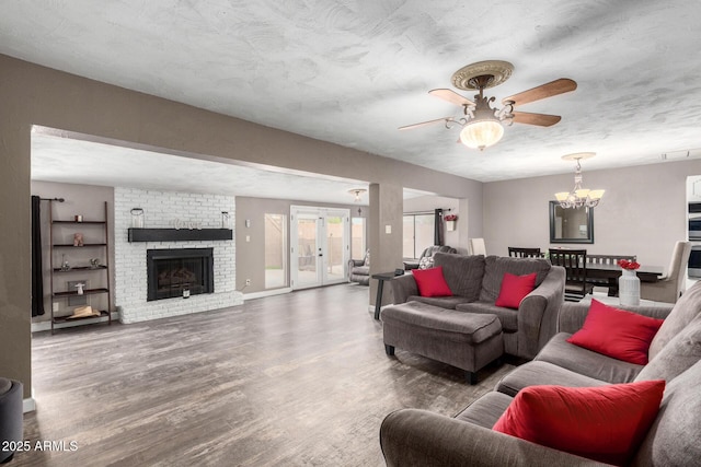 living area with french doors, a fireplace, ceiling fan with notable chandelier, and wood finished floors
