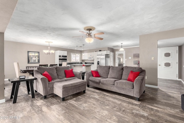 living room featuring baseboards, wood finished floors, and ceiling fan with notable chandelier