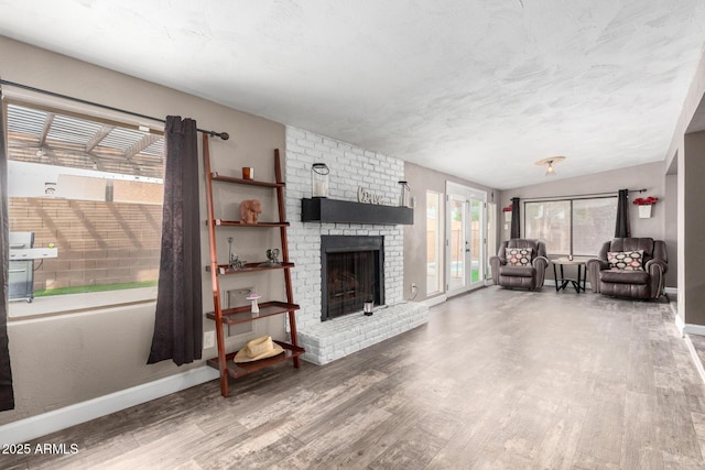 living area featuring a brick fireplace, baseboards, and wood finished floors
