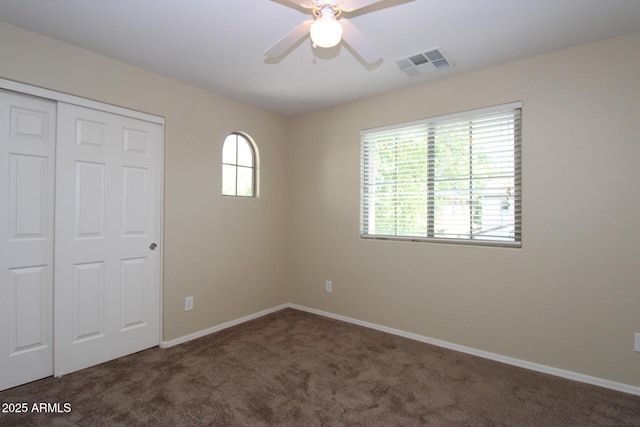 unfurnished bedroom with dark carpet, a closet, and ceiling fan