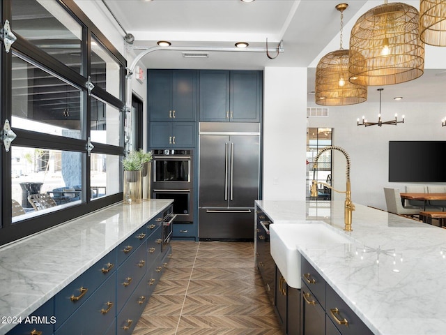 kitchen with light stone countertops, blue cabinetry, appliances with stainless steel finishes, and a sink