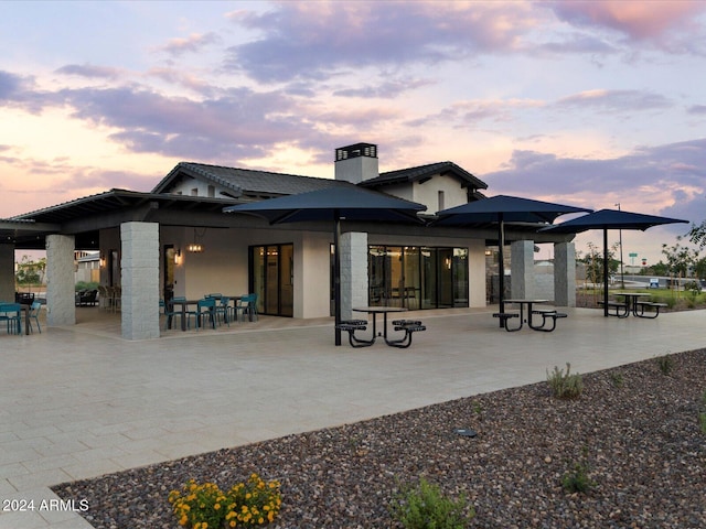 back of property at dusk with a patio area, a chimney, and stucco siding