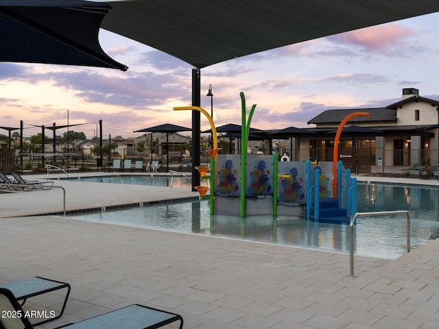 pool at dusk featuring a patio area, a community pool, fence, and a water play area