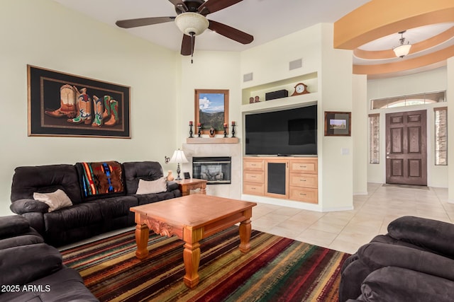 living room featuring light tile patterned floors, visible vents, a ceiling fan, built in shelves, and a fireplace