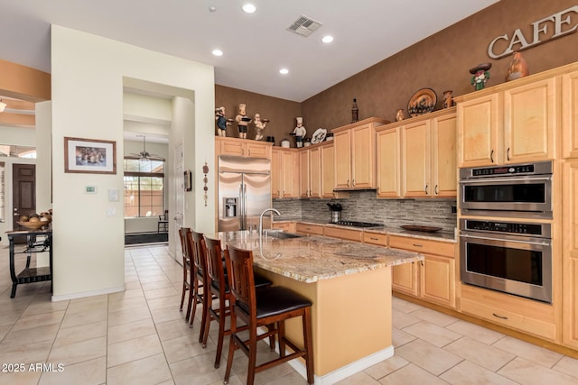 kitchen with stainless steel appliances, light brown cabinetry, a sink, and light stone counters