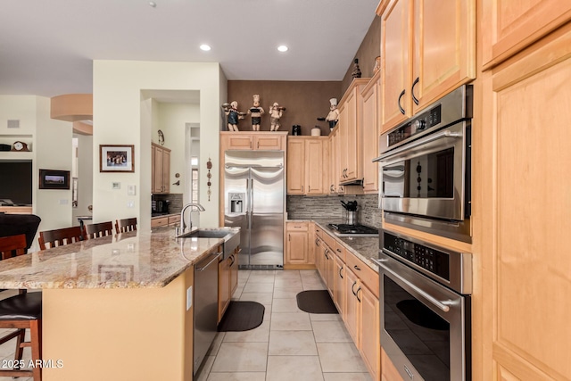 kitchen with a breakfast bar area, stainless steel appliances, light brown cabinets, a sink, and light tile patterned flooring