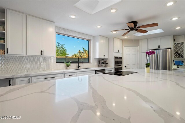 kitchen with appliances with stainless steel finishes, a sink, a skylight, white cabinets, and recessed lighting