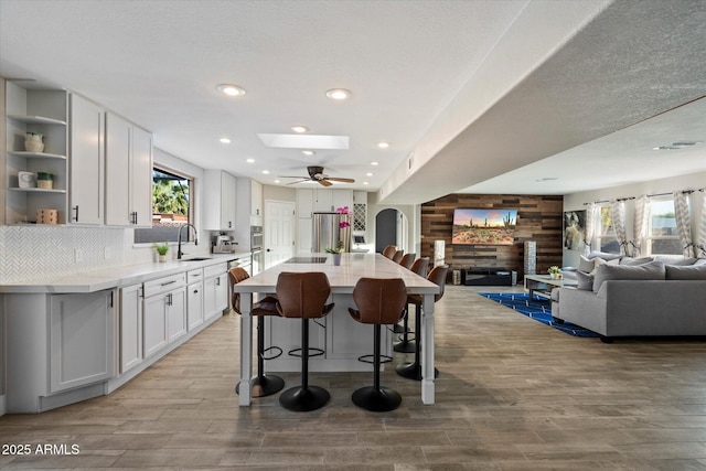 kitchen featuring a sink, appliances with stainless steel finishes, open floor plan, open shelves, and light wood-style floors
