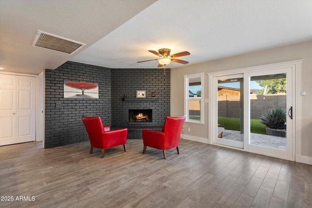 living room featuring wood finished floors, a brick fireplace, ceiling fan, and baseboards