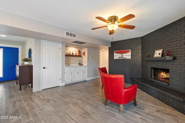 living area featuring bar, a fireplace, light wood-style floors, a ceiling fan, and baseboards
