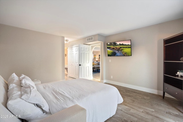 bedroom with light wood-style floors, baseboards, and arched walkways