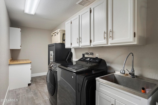clothes washing area with cabinet space, separate washer and dryer, light wood-type flooring, baseboards, and a textured ceiling